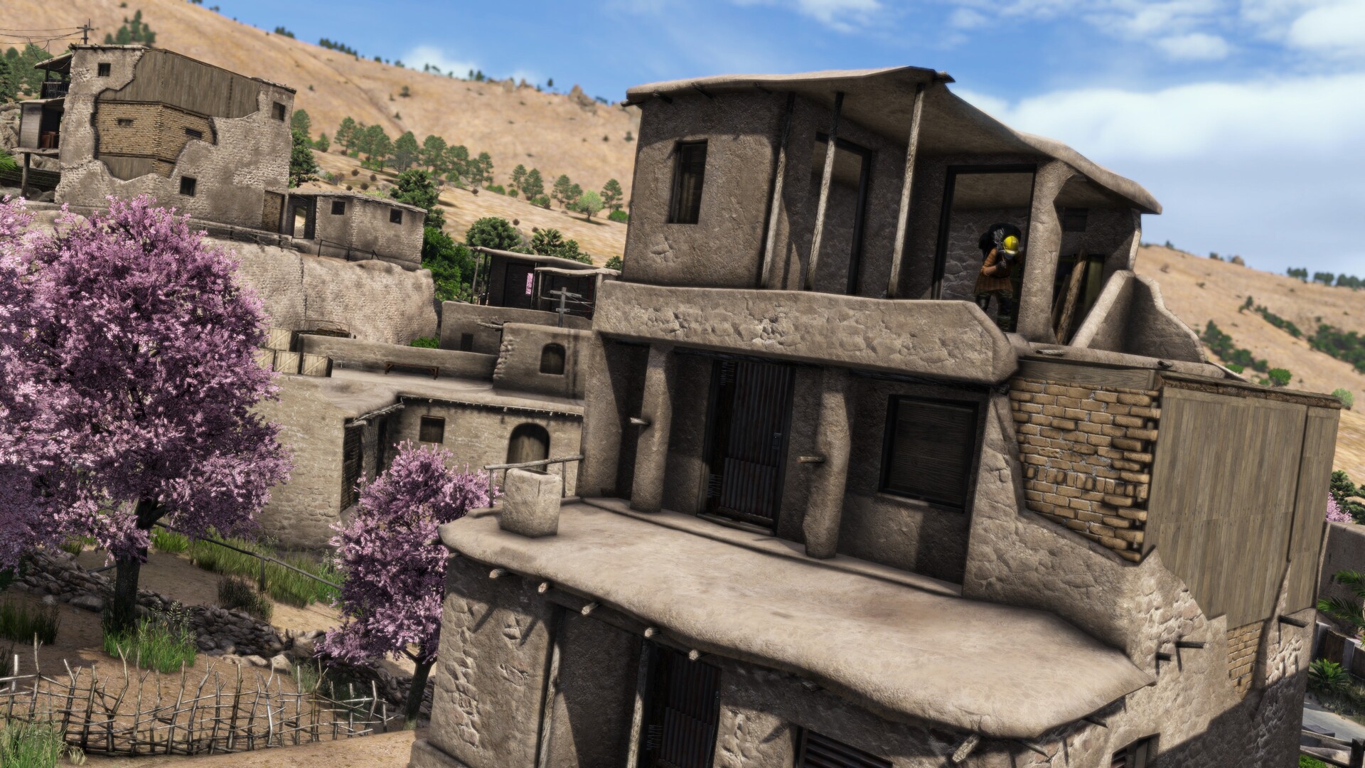 Survivor on a balcony overlooking a desert town with pink-blossomed trees in DayZ Badlands
